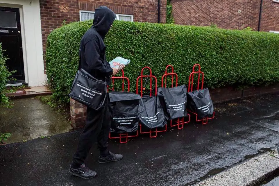 A Black & White Leaflets distributor delivering door to door, with branded GPS-tracked delivery bags lined up on the pavement